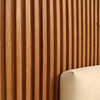 Close-up of vertical wood-grain striped peel-and-stick wallpaper on a wall next to a white cushion.