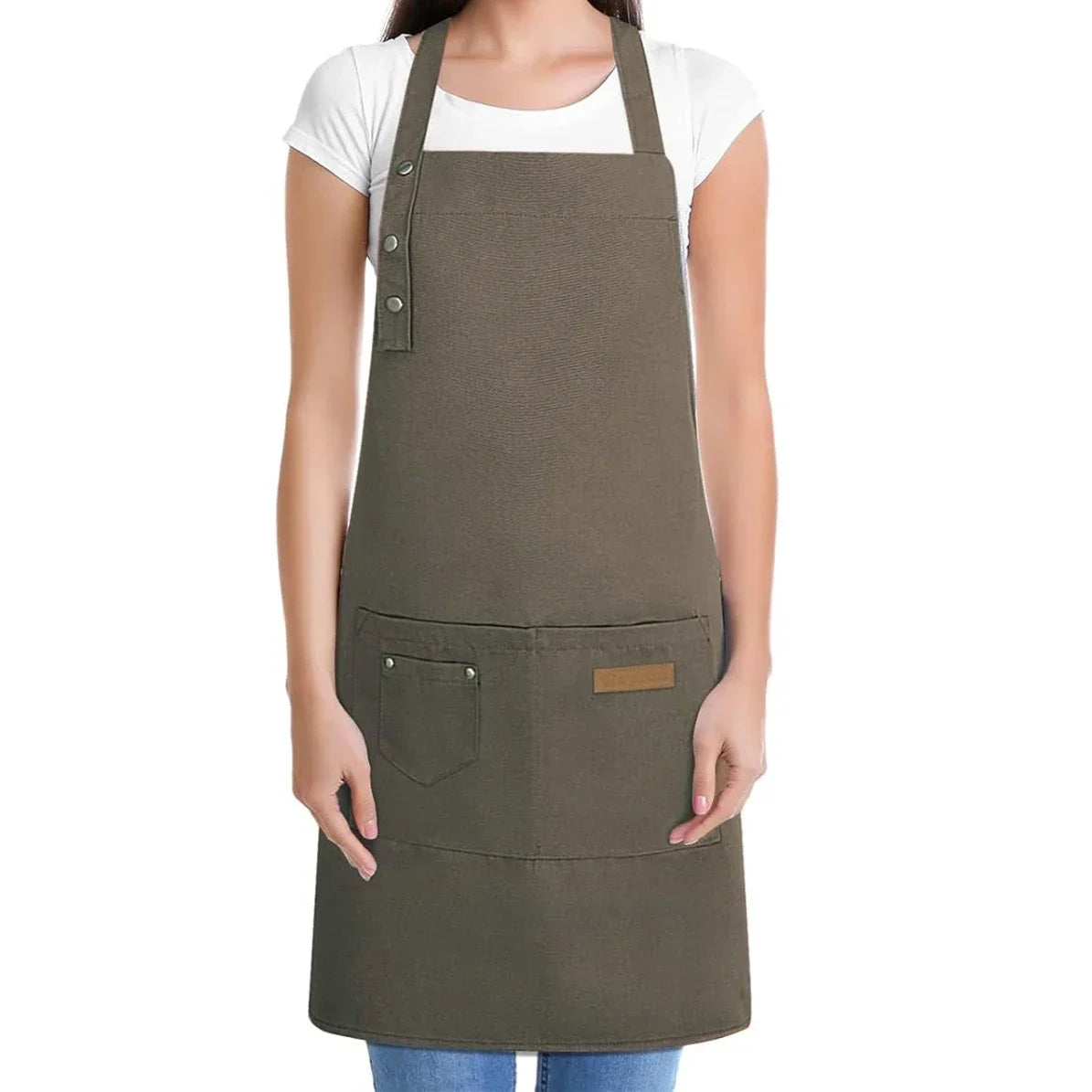 A woman is wearing a dark olive green cotton canvas apron with multiple pockets over a white shirt.