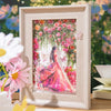 A framed watercolor illustration of a woman surrounded by pink and red roses and greenery.