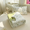 A collection of white and green patterned pillows and a folded duvet cover on a light-colored surface.