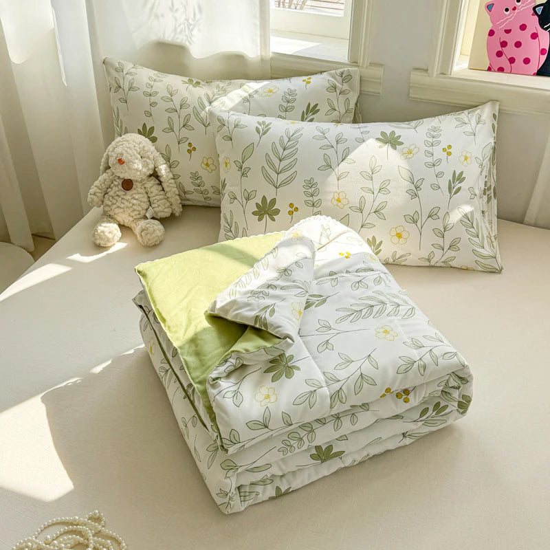 A collection of white and green patterned pillows and a folded duvet cover on a light-colored surface.