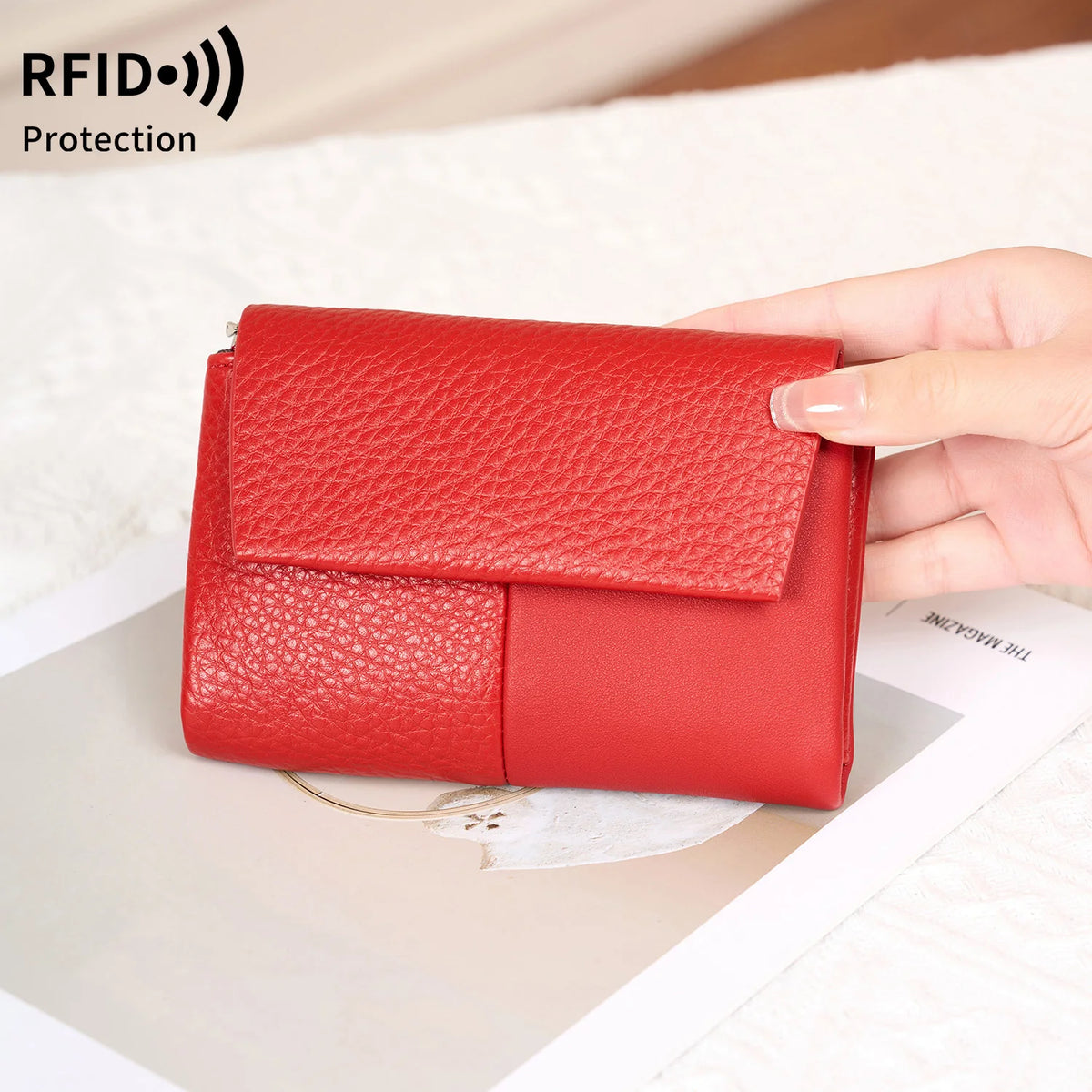 A red RFID-blocking tri-fold wallet with a zipper pocket is held in a person's hand on a light surface.