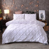 White queen comfort bedding set featuring a quilted comforter and pillows against a gray wall.