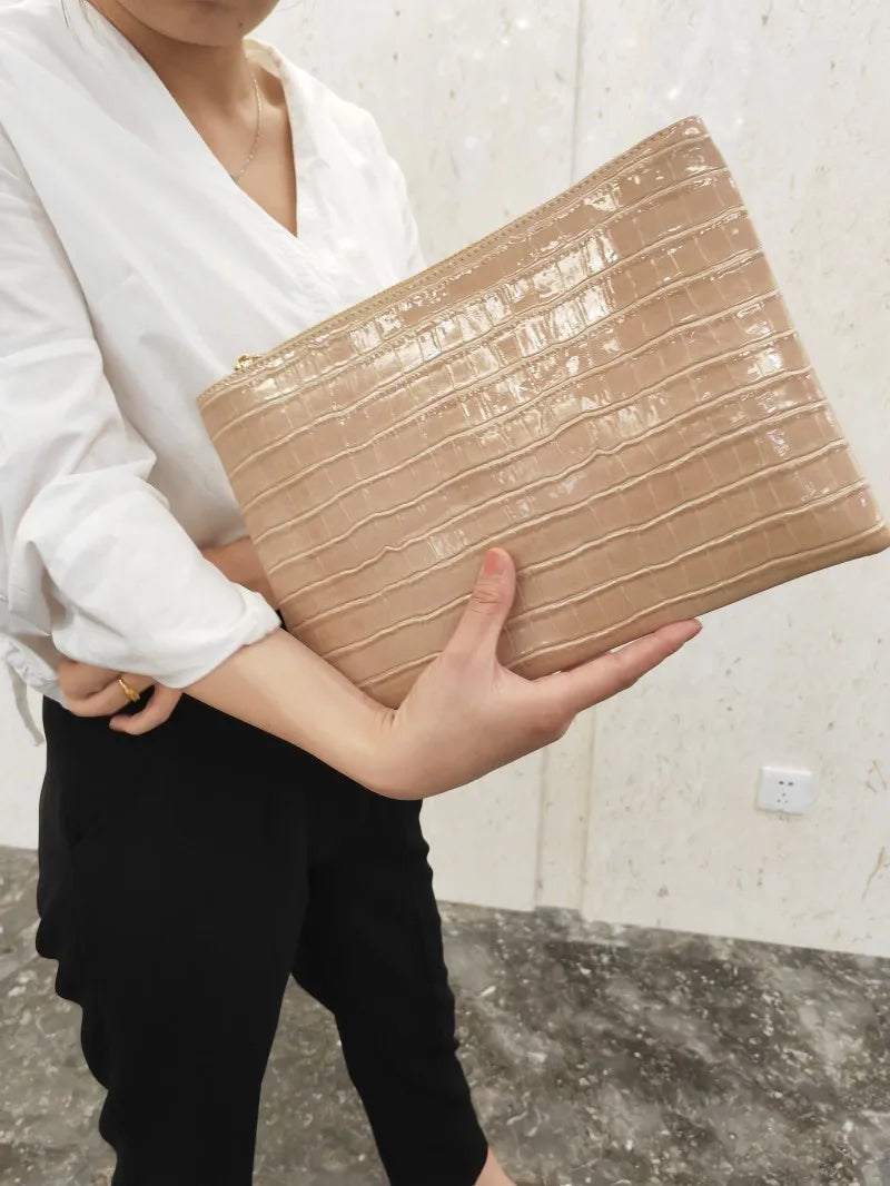 A woman holds a beige crocodile-embossed PU leather envelope clutch against a light background.