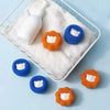 A white mesh basket holds several reusable laundry balls in orange and blue colors on a white towel.