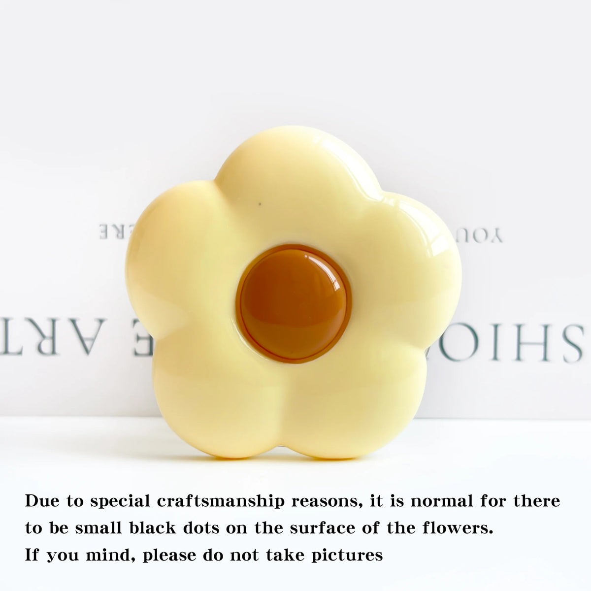 A pale yellow flower-shaped phone grip stand with small black dots on the surface.