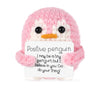 A handmade knitted pink penguin doll with a white card that reads Positive penguin I may be a tiny penguin but I believe in y