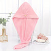 A pink microfiber towel wrap for hair is displayed on a glass stand next to a potted plant.