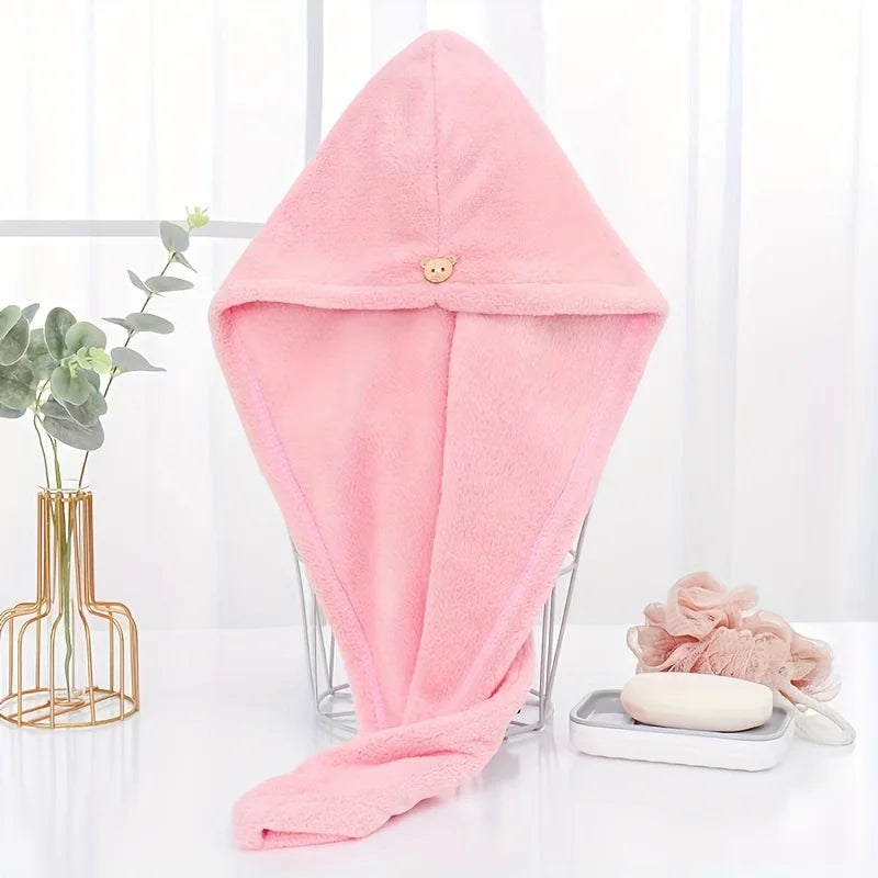 A pink microfiber towel wrap for hair is displayed on a glass stand next to a potted plant.