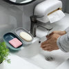 A hand is using a leaf-shaped suction cup soap dish on a white bathroom sink with a modern faucet.
