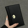 A hand holds a sleek black compact wallet with a gold embossed logo against a gray background.