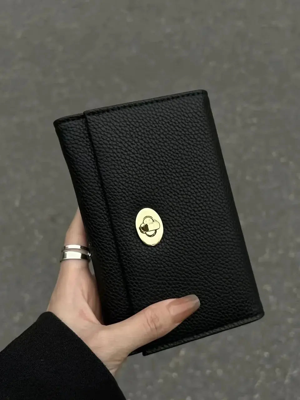 A hand holds a sleek black compact wallet with a gold embossed logo against a gray background.