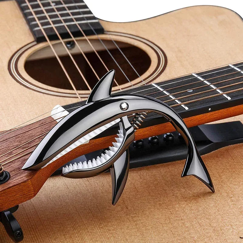 A close-up of a guitar fret with a shark-design capo made of zinc alloy resting on the wood.