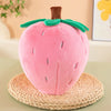 A pink strawberry plush throw pillow resting on a woven mat.