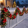 A white picket fence decorated with red and green LED Christmas garlands in a snowy outdoor setting.