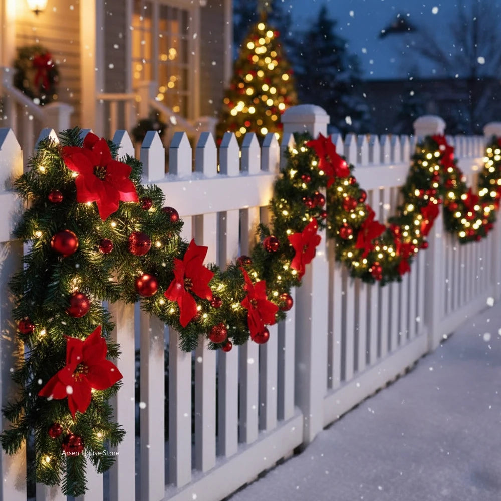 A white picket fence decorated with red and green LED Christmas garlands in a snowy outdoor setting.