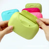 A hand holds a lime green portable soap holder with a lid, surrounded by other colored versions.