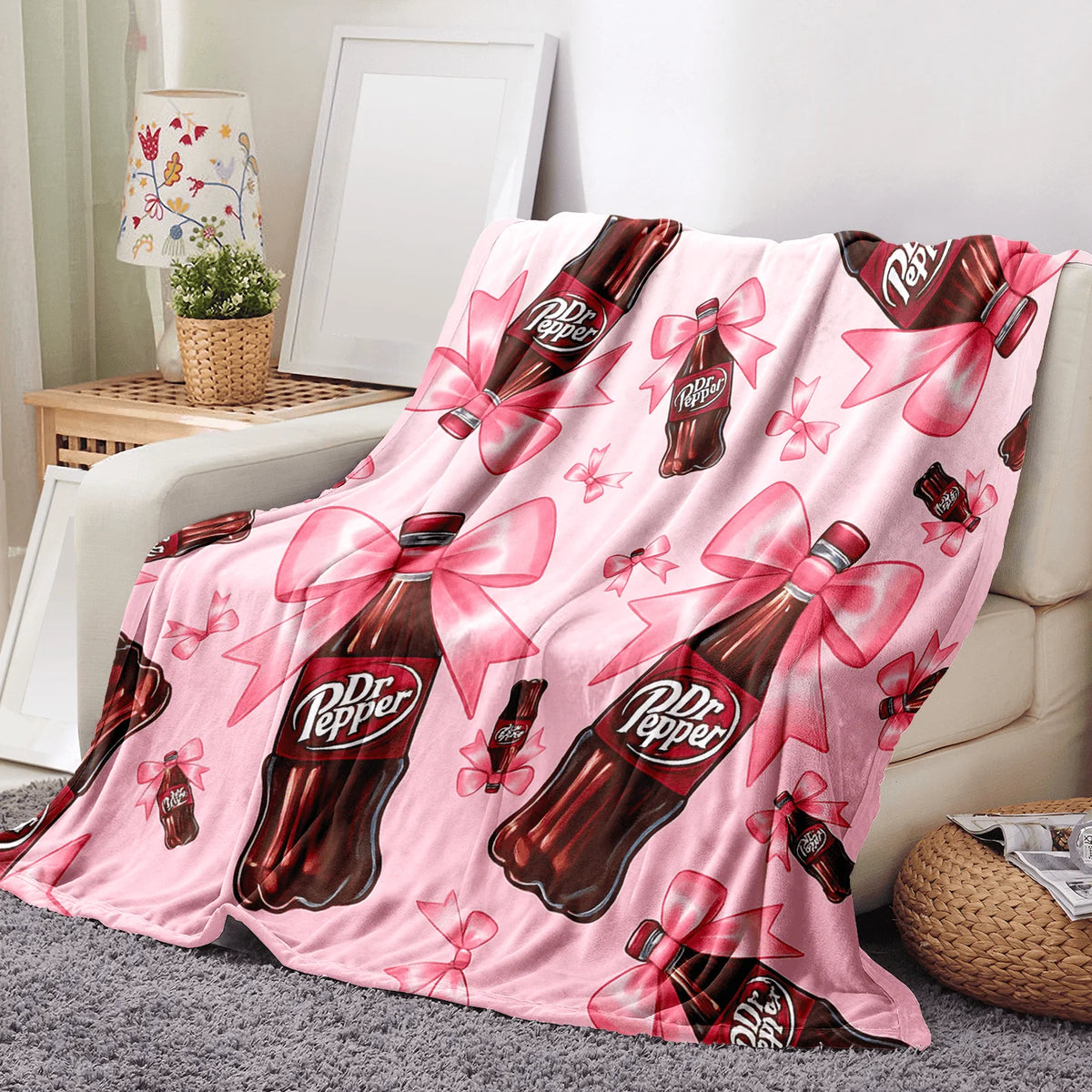 A pink throw blanket featuring a repeating pattern of Dr. Pepper bottles tied with pink ribbons.