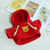 A bright red knitted hoodie with a yellow bear patch detail, displayed on a white wooden surface.