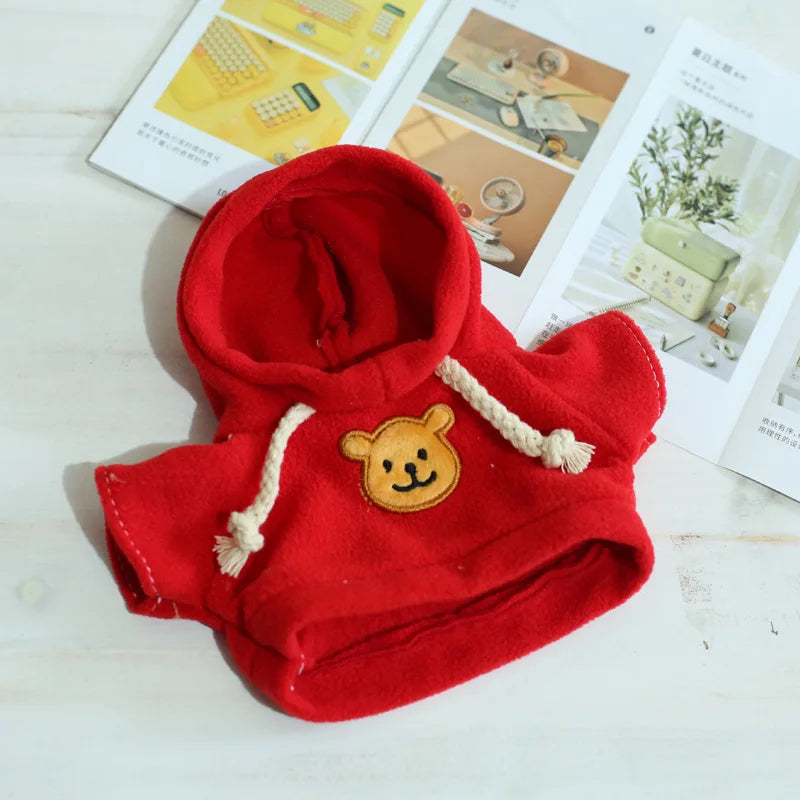 A bright red knitted hoodie with a yellow bear patch detail, displayed on a white wooden surface.