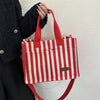 A person holds a red and white striped canvas tote bag with inner pockets against a light background.