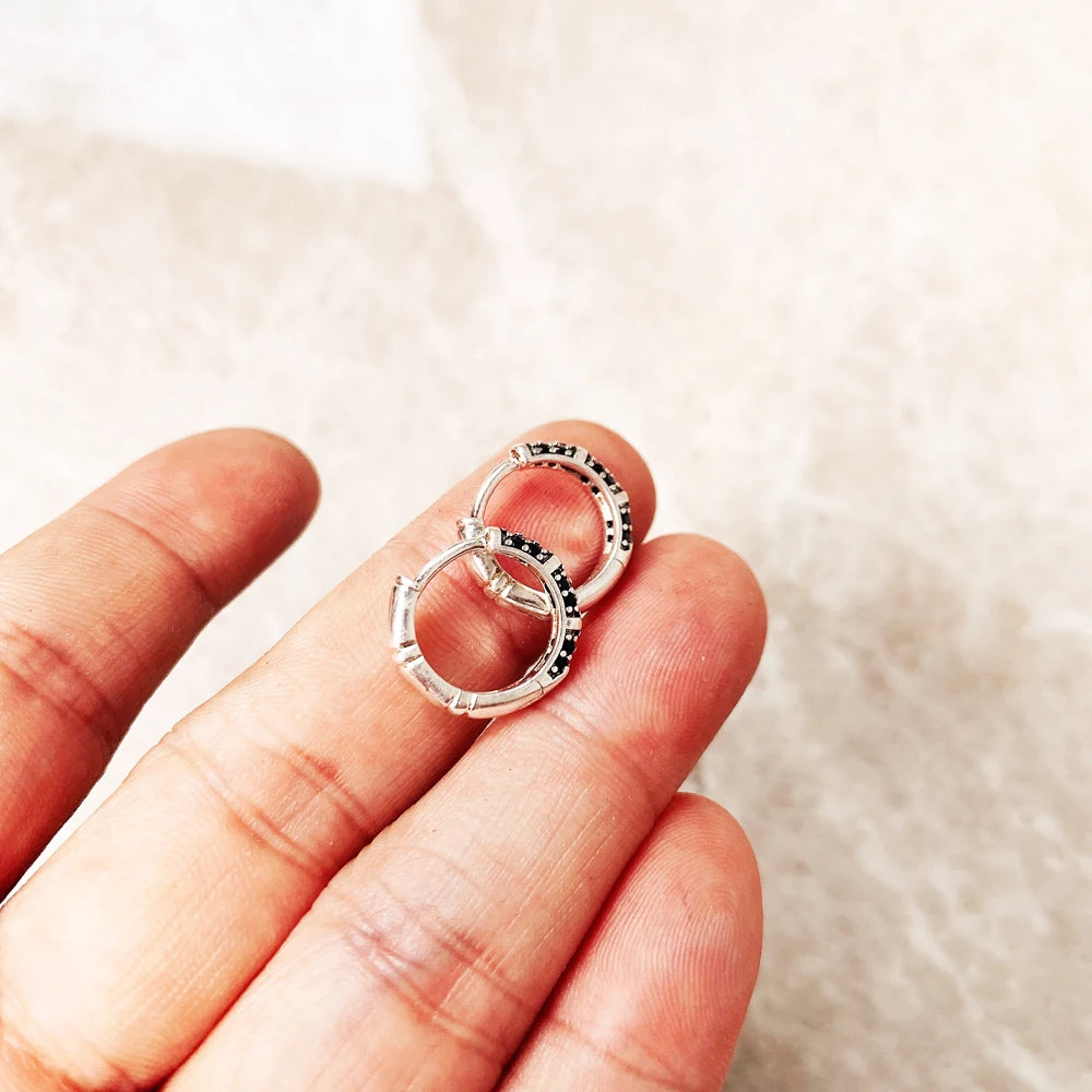 A hand holds a pair of bamboo-style hinged hoop earrings in sterling silver.