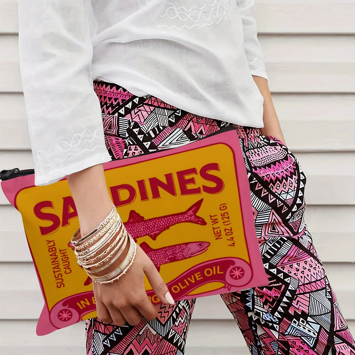 Une main tient une pochette de maquillage jaune avec un design d'huile d'olive vintage sur une tenue à motifs roses.