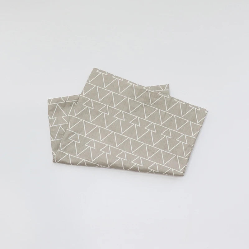 A stack of soft cotton baby pillowcases featuring a geometric cartoon pattern in beige and white.