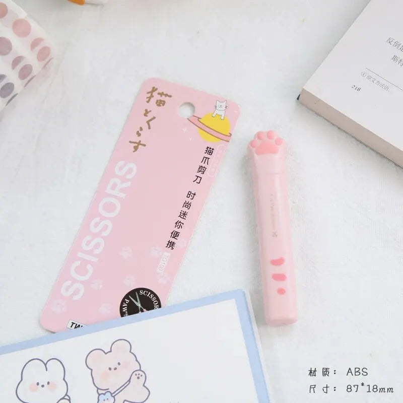 Pink portable scissors with a cat paw design and an ABS packaging card are shown on a white surface.
