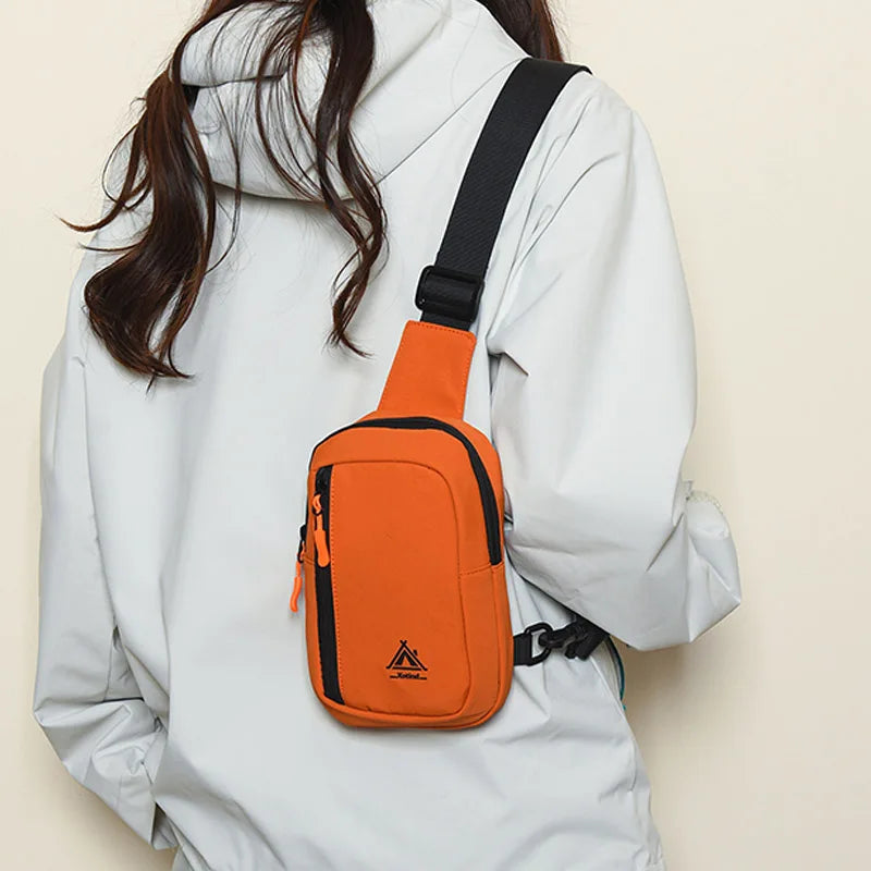 An orange water-resistant nylon chest sling bag worn on a person's white jacket.
