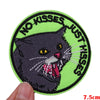 A round embroidered patch featuring a black cat with yellow eyes and the text NO KISSES JUST HISSES in green.