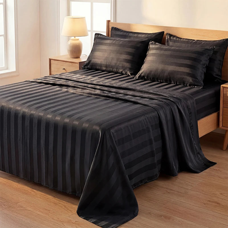 A black and gray striped satin bed sheet set is draped over a wooden bed with a lamp in the background.