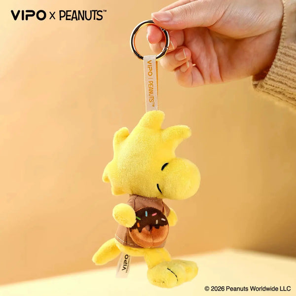 A yellow Snoopy plush keychain hanging from a silver ring, shown being held by a hand.