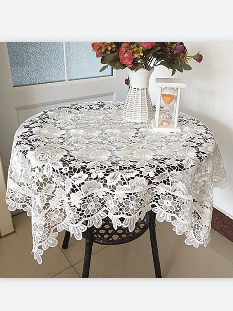 White lace tablecloth with embroidered rose design set on a table.