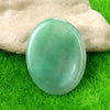 A smooth, oval green crystal stone resting on bright green grass, held by a hand.