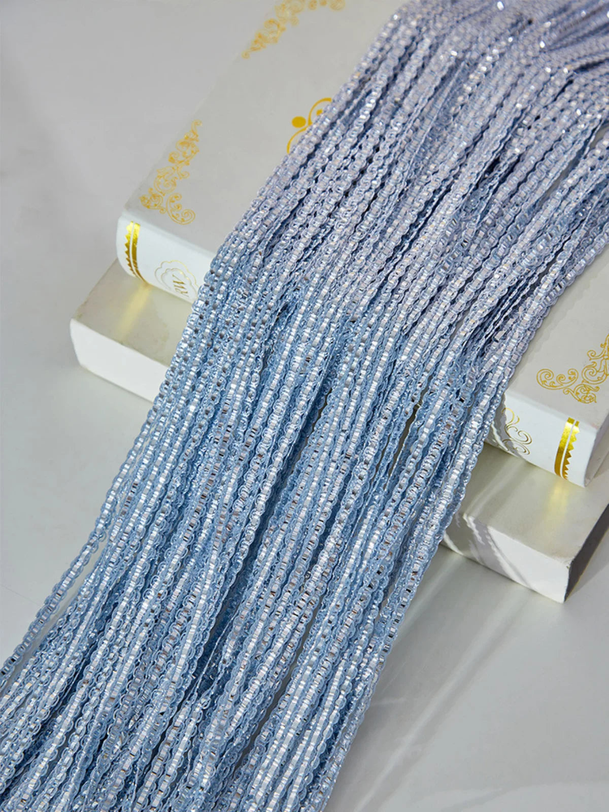 A close-up of a long strand of light blue silver tassel string curtain hanging next to a white box.