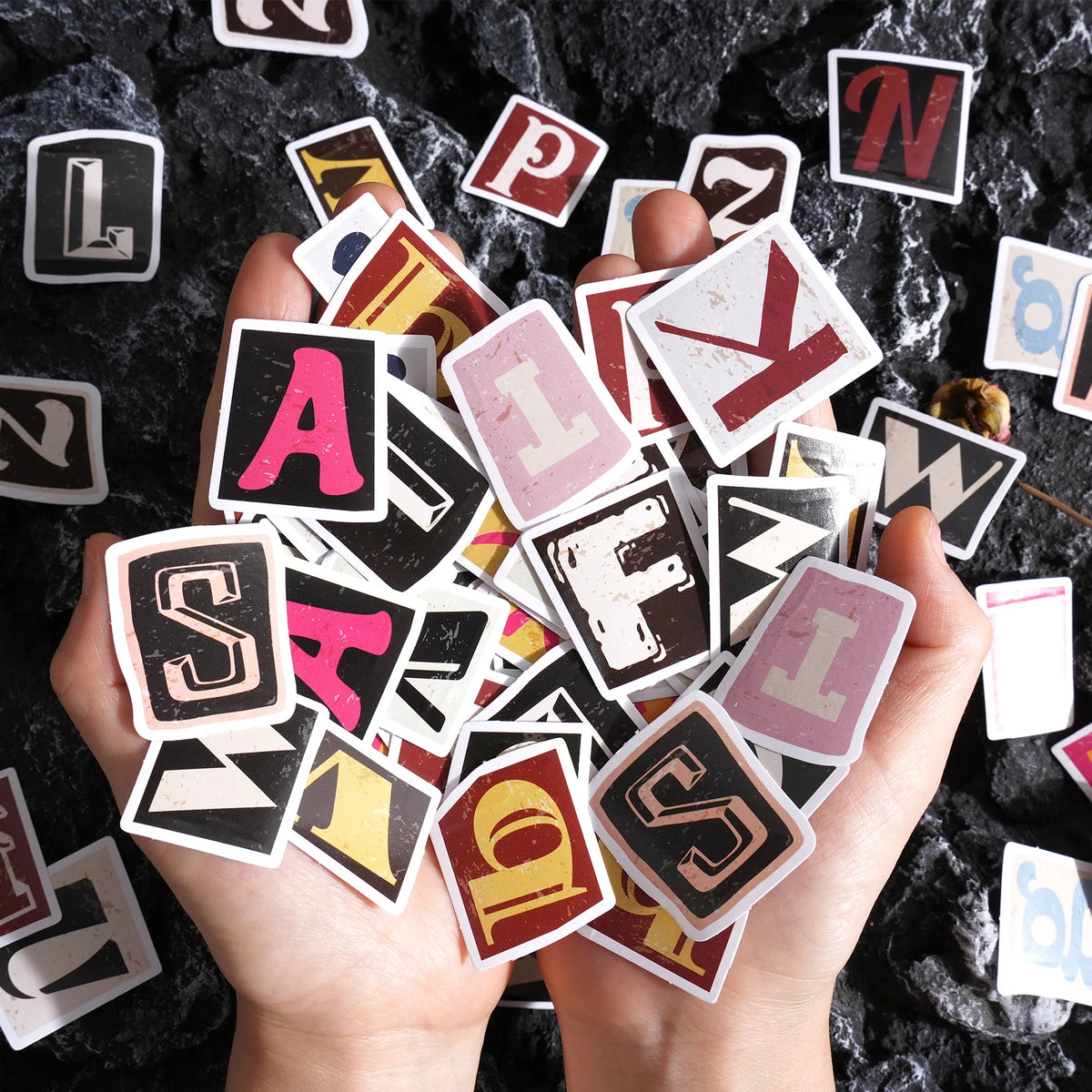A hand holds a collection of vintage alphabet stickers on a dark surface.