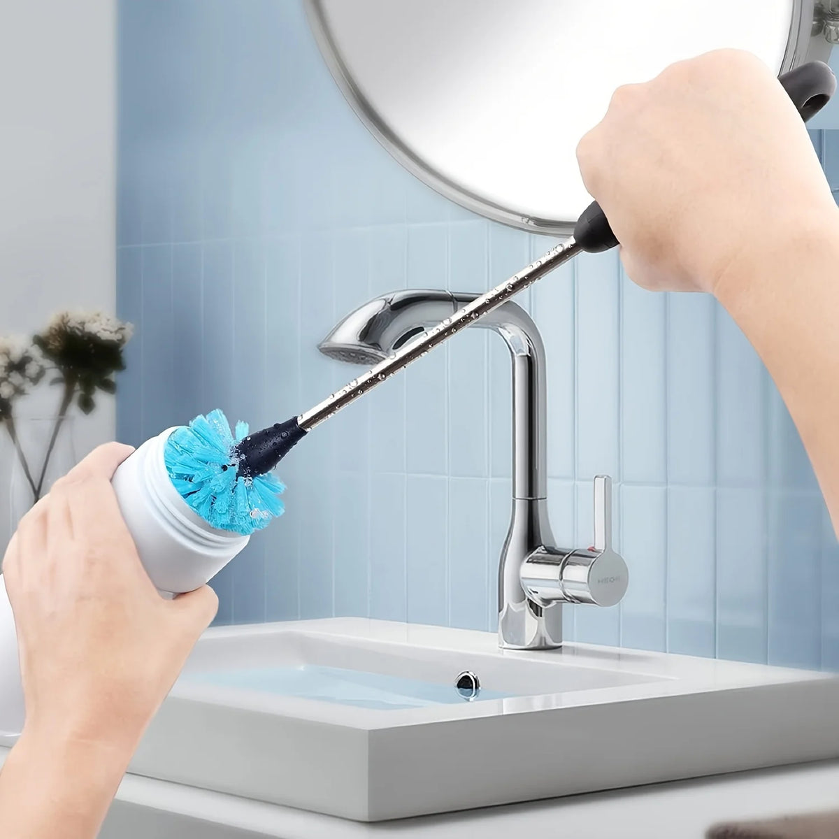 A hand is using a long, flexible bottle cleaning brush with a blue bristles to clean a kitchen faucet.