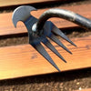 A close-up of a durable manganese steel hand weeder with sharp, pointed tines against a wooden background.