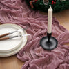 A festive table setting featuring a white candle and silverware on a pink crinkle gauze cheesecloth runner.