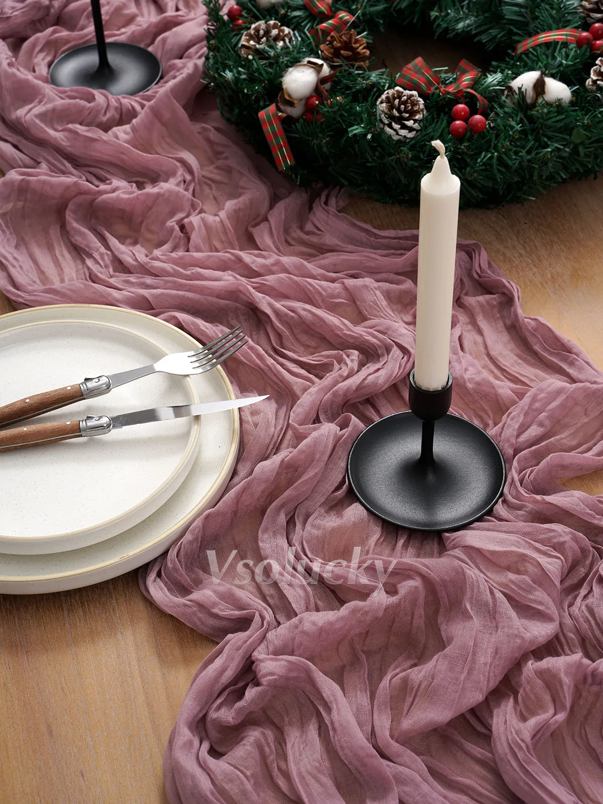 A festive table setting featuring a white candle and silverware on a pink crinkle gauze cheesecloth runner.
