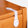 A white adhesive baby proofing latch is attached to a wooden cabinet drawer, used for child safety.