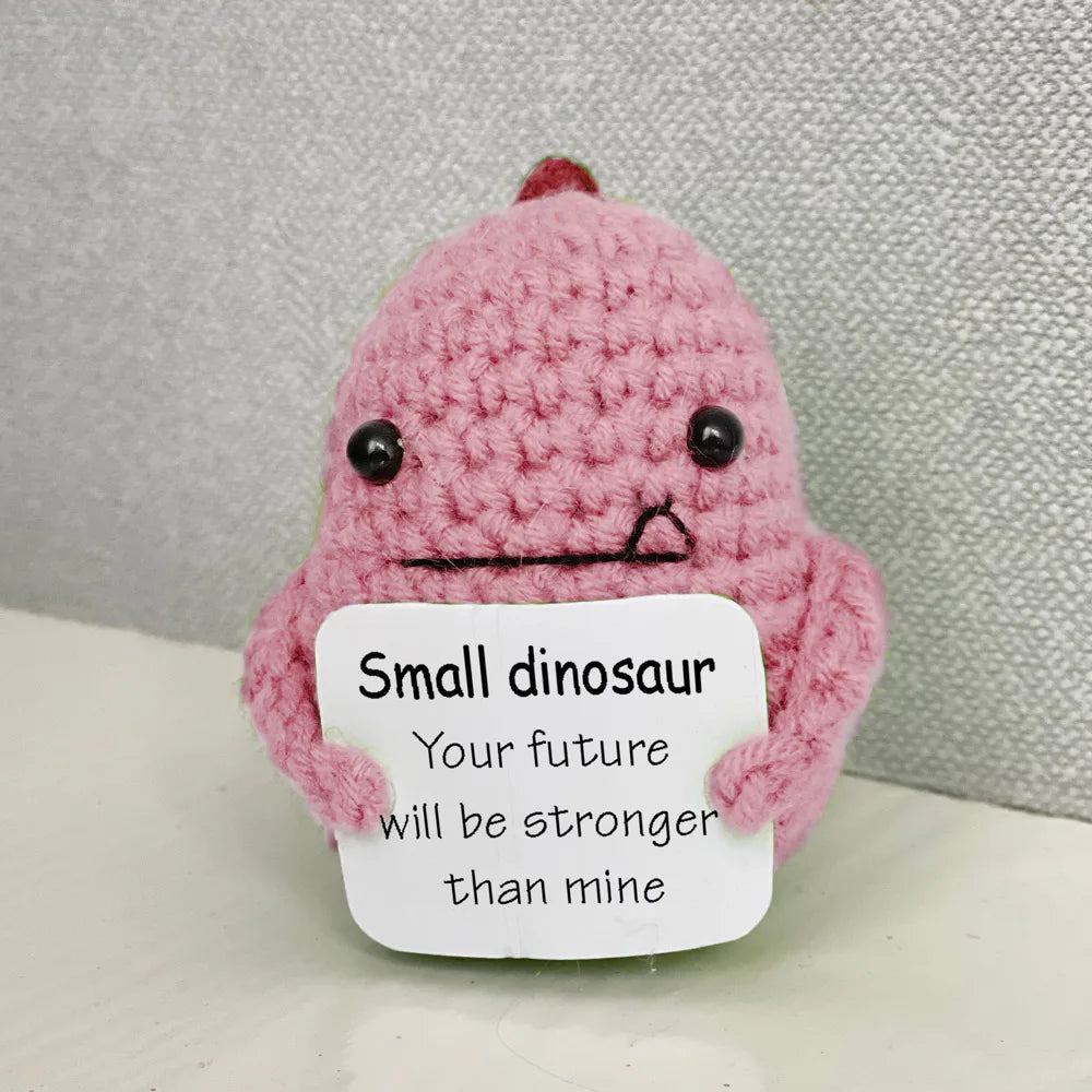A handmade pink crochet dinosaur doll with a sad expression and a note that says Small dinosaur Your future will be stronger 