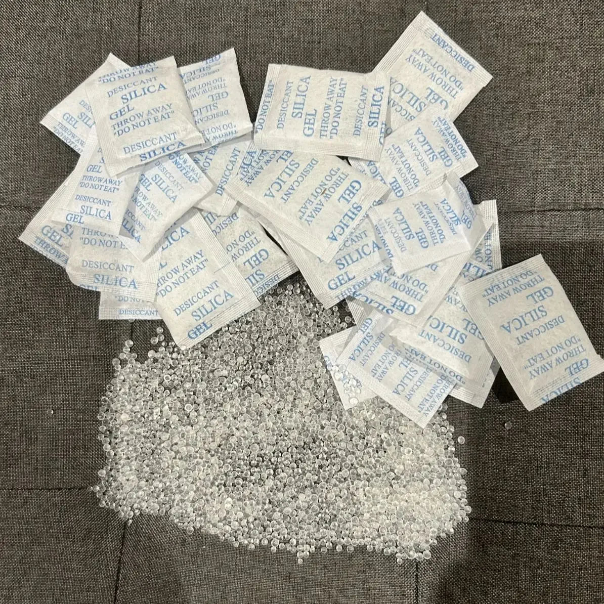 Small white silica gel moisture absorber bags scattered on a dark surface.