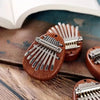 A close-up of a wooden kalimba thumb piano with metal tines resting on a brown fabric surface.