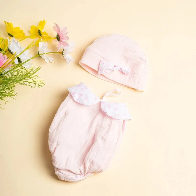 A pink 3-piece doll outfit set for a baby doll, including a hat and pants, with yellow and pink flowers nearby.