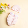 A pink 3-piece doll outfit set for a baby doll, including a hat and pants, laid on a light background with flowers.