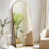 A full length mirror with a gold frame reflects a potted palm plant in a bright, modern interior.