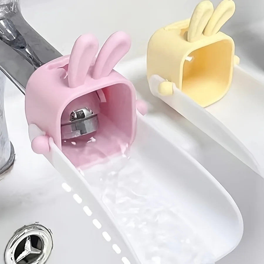 A pink rabbit-themed anti-splash faucet extender is shown dispensing water into a white dish.