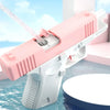 A pink and white water blaster pistol is shown spraying water in an outdoor setting.